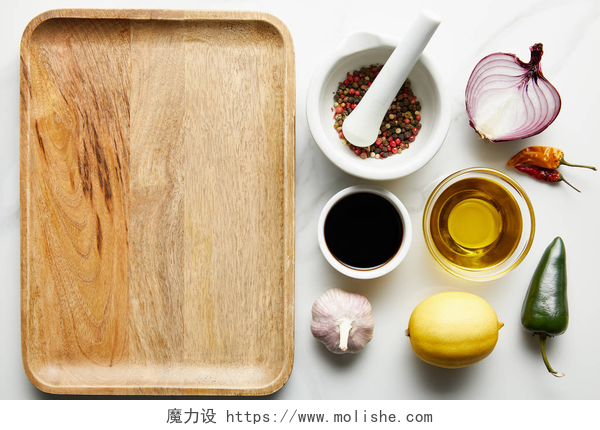 白色桌上的木质盘子和调味料俯视图酱油、橄榄油、调味品和柠檬在大理石底板旁边的俯瞰图